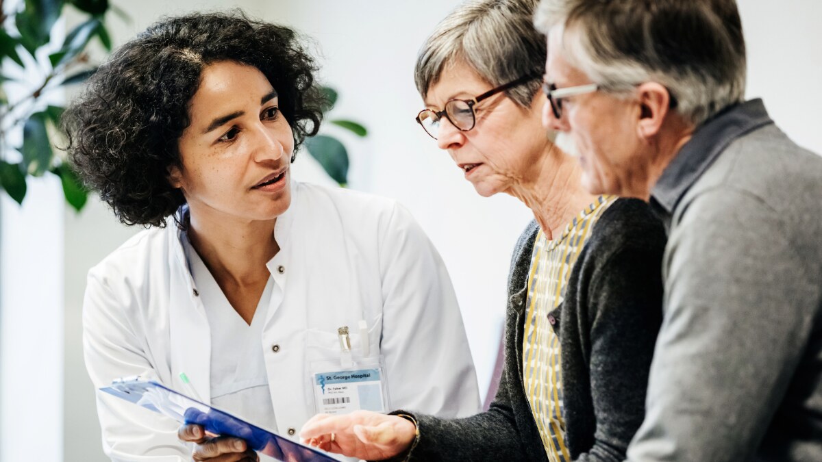 a female doctor holding a chart and explaining something to a woman and a man